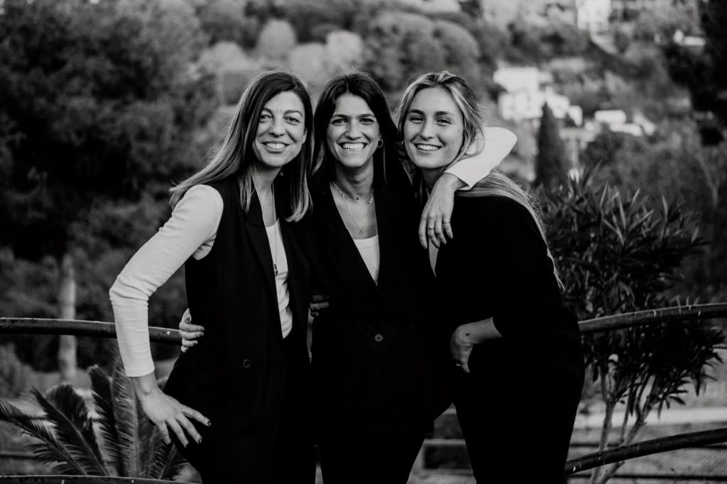Las tres Wedding Planners de La Finka 4.1 posan juntas en espacios ajardinados junto a sus materiales de Event Planning, preparando bodas y eventos corporativos en Barcelona.